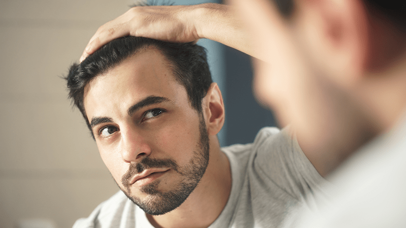 A man looks at his receding hairline in the mirror.